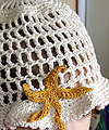 Starfish 'Skull Cap' summer hat crocheted in white craft cotton yarn, with 3D starfish motif crocheted in sand-coloured mercerised cotton yarn